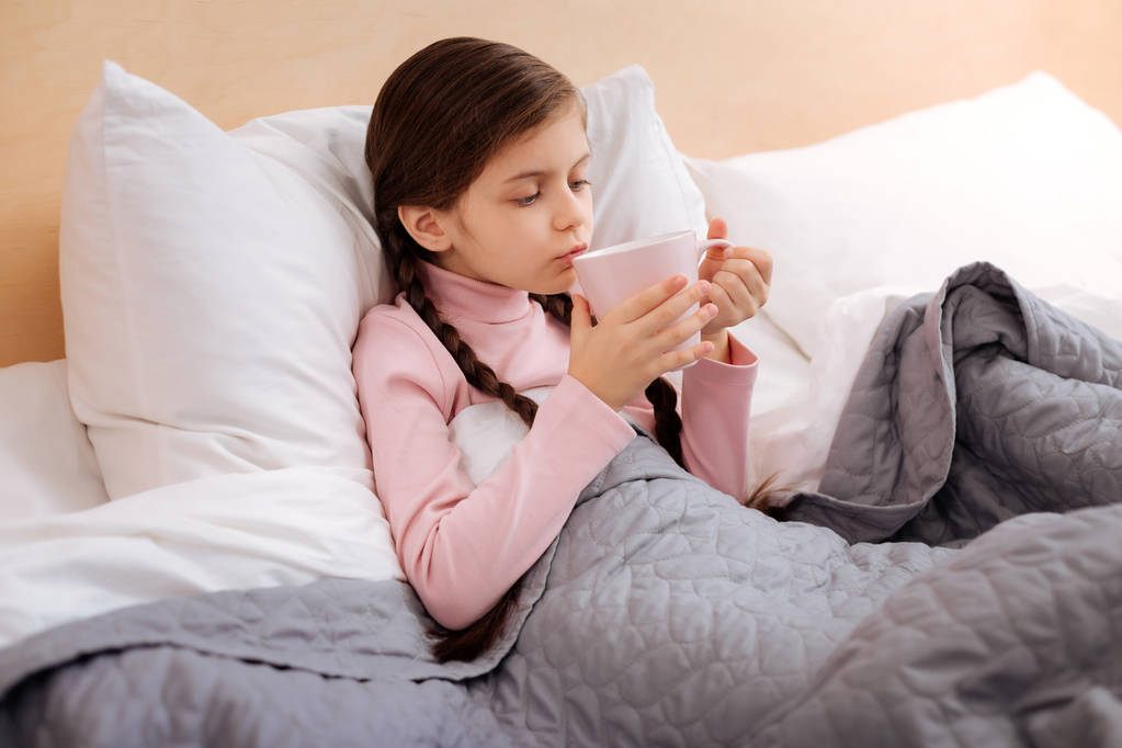 Маленькая девочка пьет чай в теплой постели
 - Фото, изображение