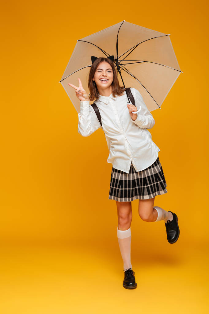 Porträt eines lustigen, glücklichen Schulmädchens in Uniform mit Regenschirm - Foto, Bild