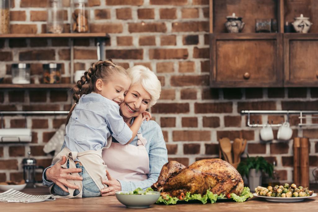 isoäiti ja lapsenlapsi syleilee keittiössä
 - Valokuva, kuva