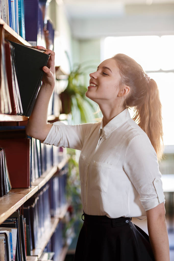 Un estudiante tomando un libro de un estante en la biblioteca
. - Foto, Imagen
