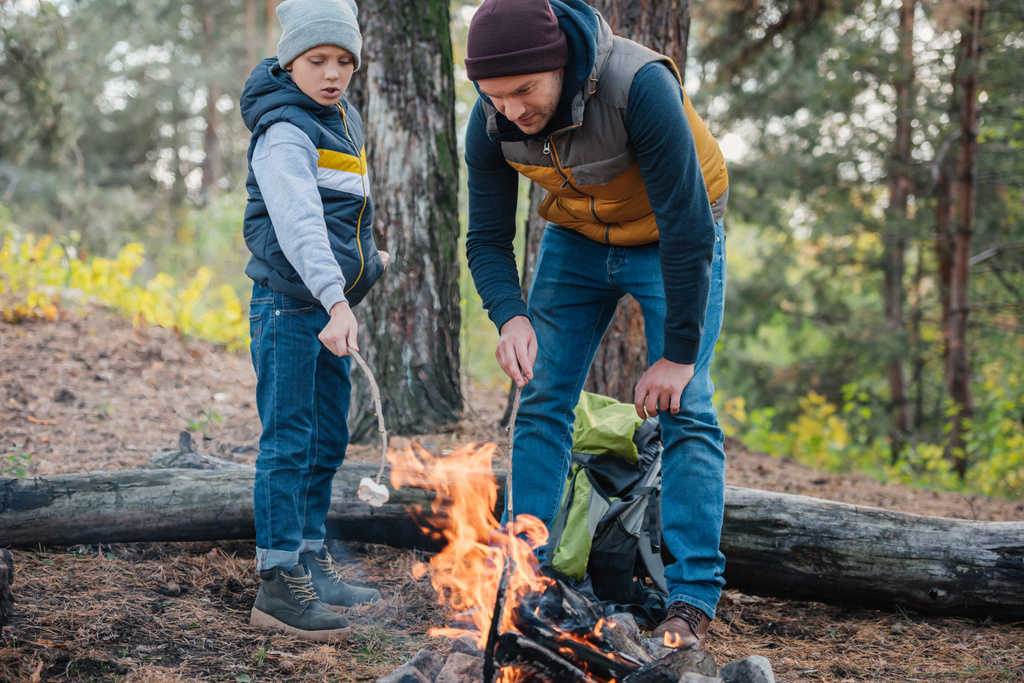 πατέρας και γιος μαγείρεμα marshmallows στο δάσος - Φωτογραφία, εικόνα