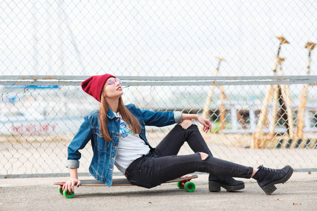 自然の背景に屋外スケート ボード上に座っているきれいな女の子. - 写真・画像