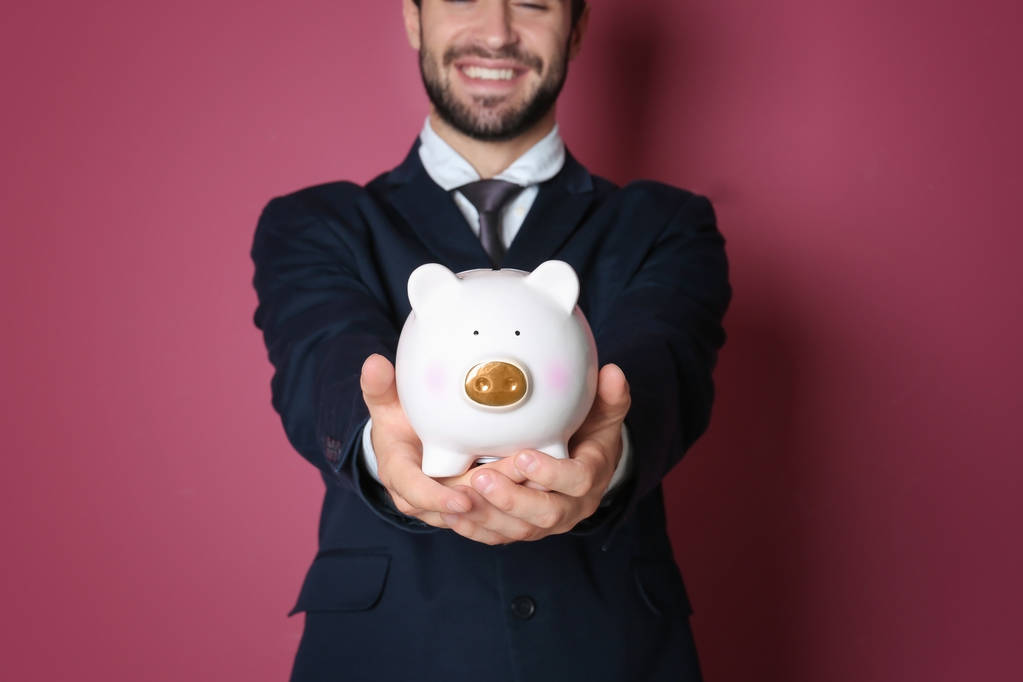 Young man with piggy bank on color background - Photo, Image