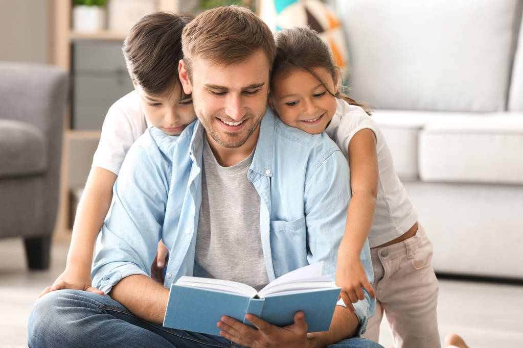 Молодой человек и его маленькие дети читают дома книги
 - Фото, изображение