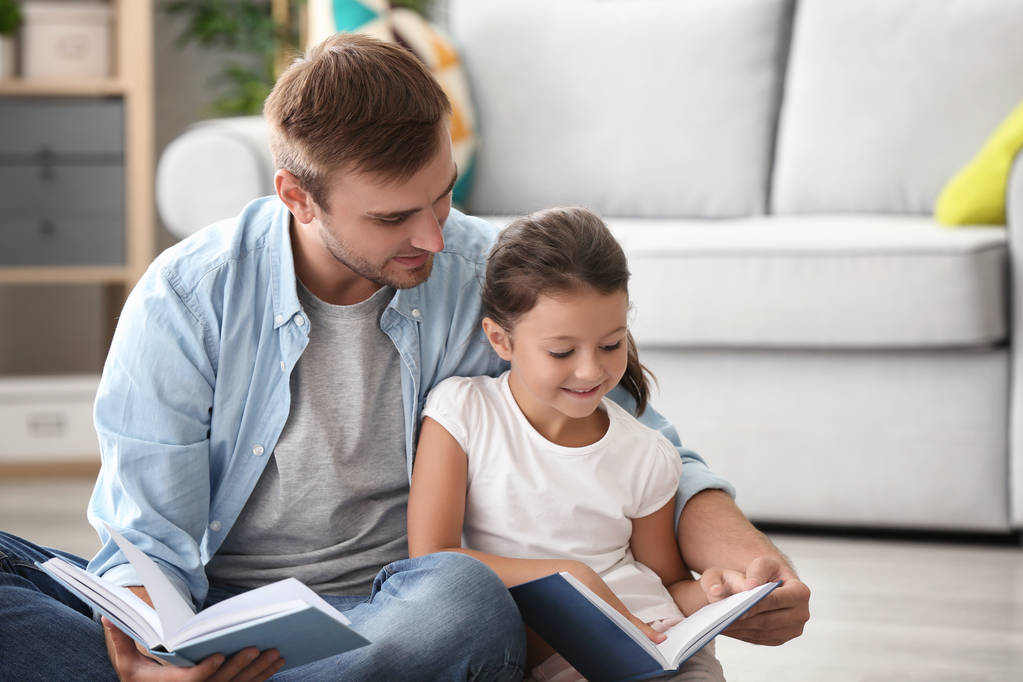 Молодий чоловік і його маленька дочка читають книгу вдома
 - Фото, зображення