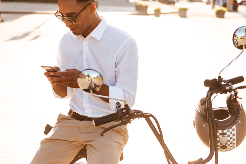 Młody człowiek Afryki w okulary, siedząc na nowoczesne motocykl na zewnątrz - Zdjęcie, obraz