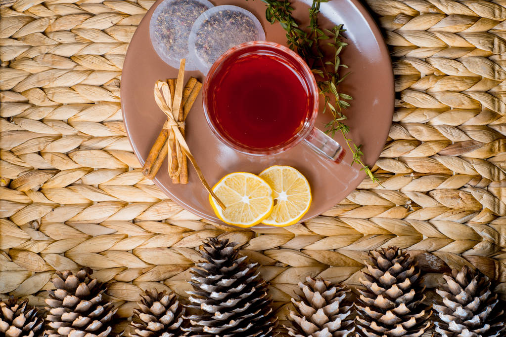Трав'яний чай з корицею і лимоном на плетеному кошику. Різдвяні шишки
 - Фото, зображення