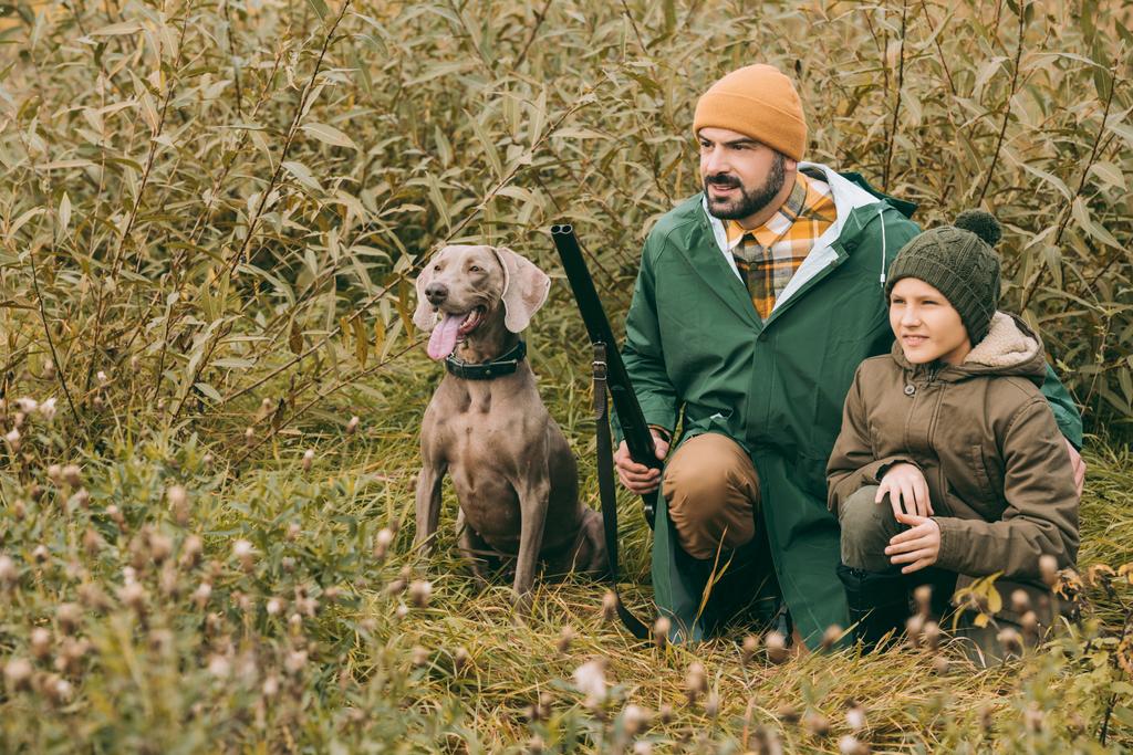 Ojciec i syn, w kucki w krzakach na polowanie - Zdjęcie, obraz