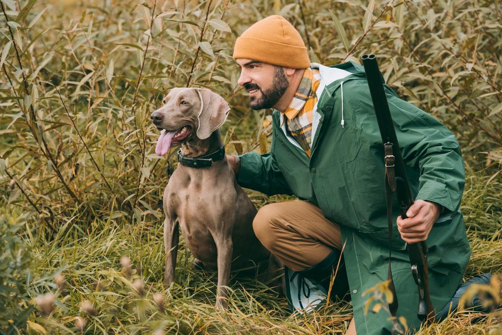 man squatting in bushes with dog and gun - Photo, Image