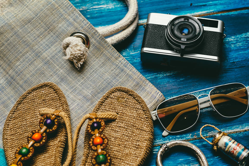 Pose plate de la mode d'été avec des pantoufles de caméra lunettes de soleil et autres accessoires fille sur fond bleu en bois
 - Photo, image