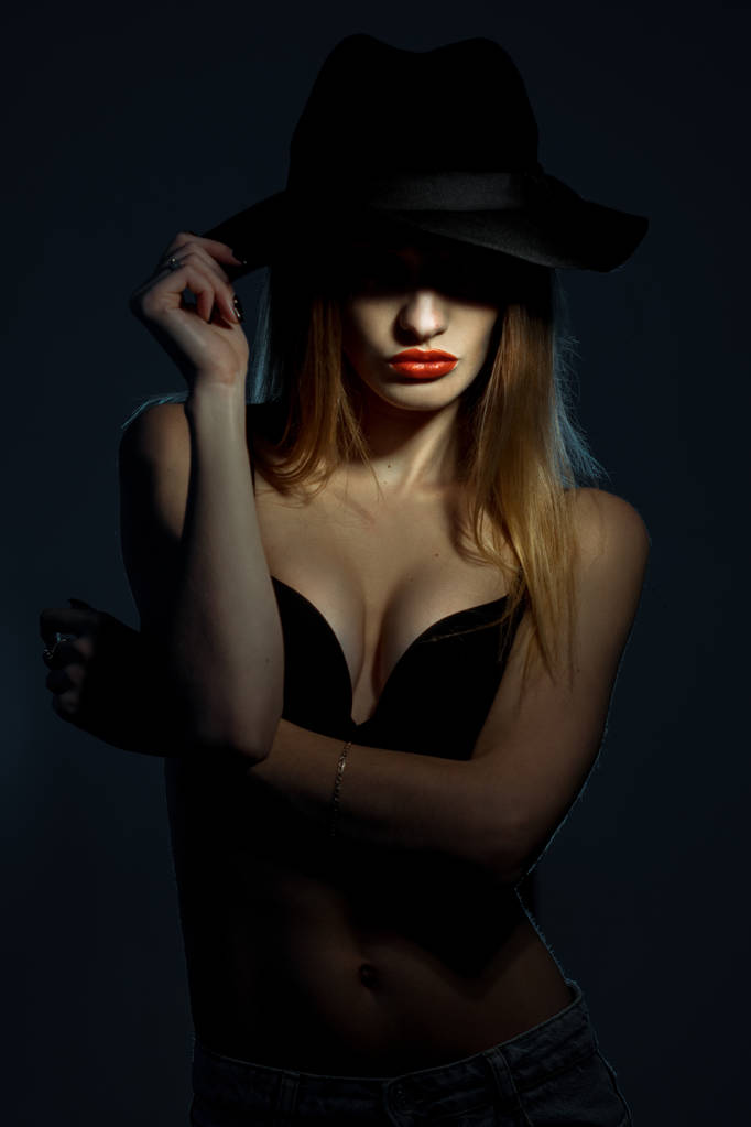 retrato de niña en sujetador negro con labios rojos usando un sombrero con ala ancha en el estudio
 - Foto, Imagen