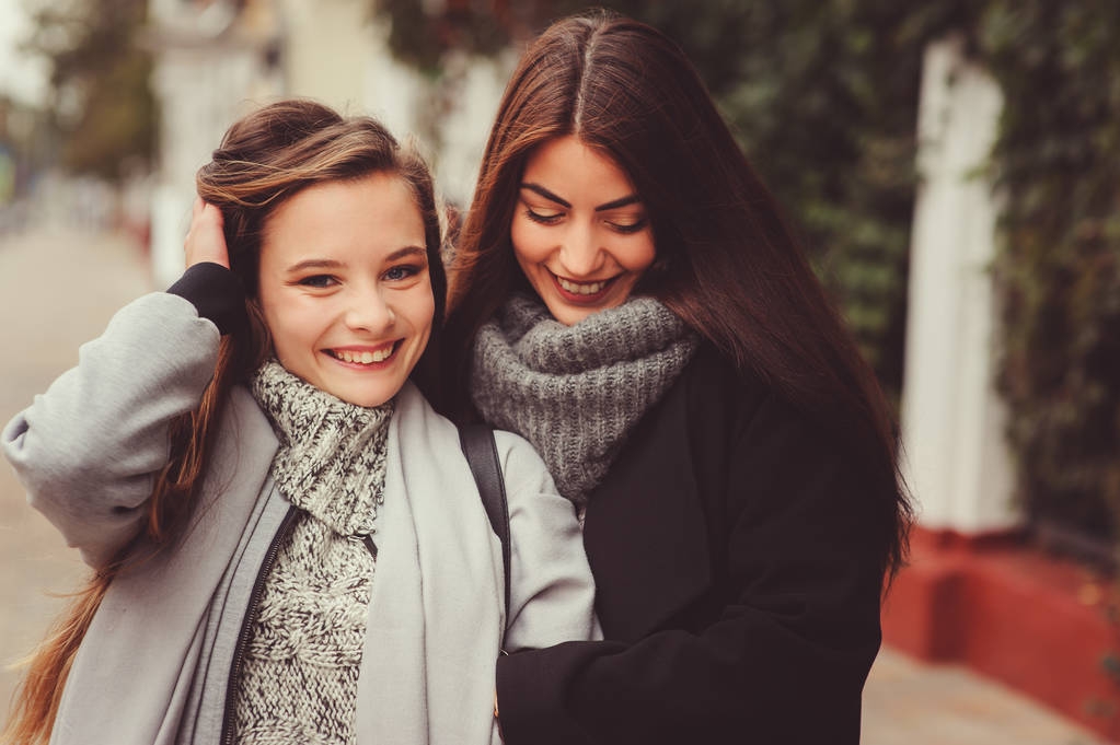 zwei junge, glückliche Freundinnen, die in lässigen Outfits durch die Straßen der Stadt laufen, warme Mäntel tragen und Spaß haben - Foto, Bild