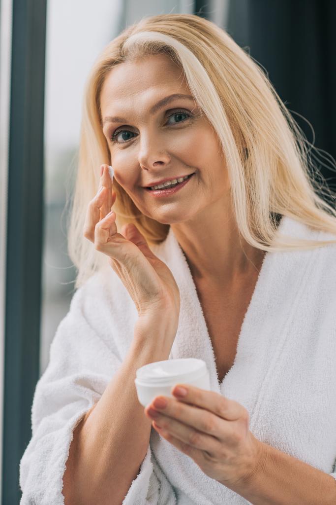 mujer madura aplicando crema cosmética
 - Foto, Imagen