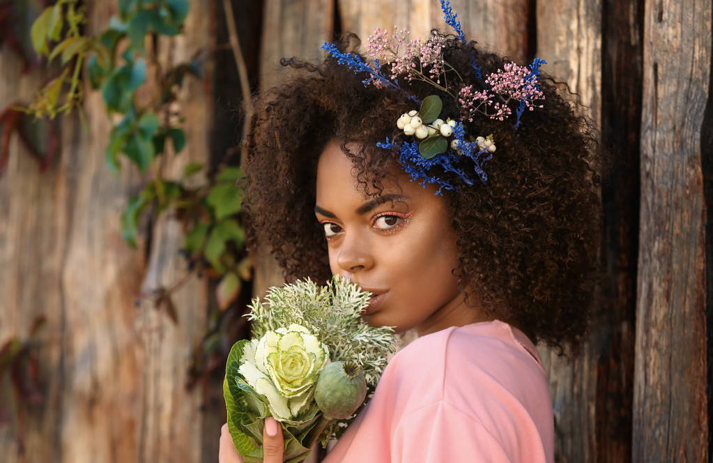 Bela jovem afro-americana com flores contra fundo de madeira
 - Foto, Imagem