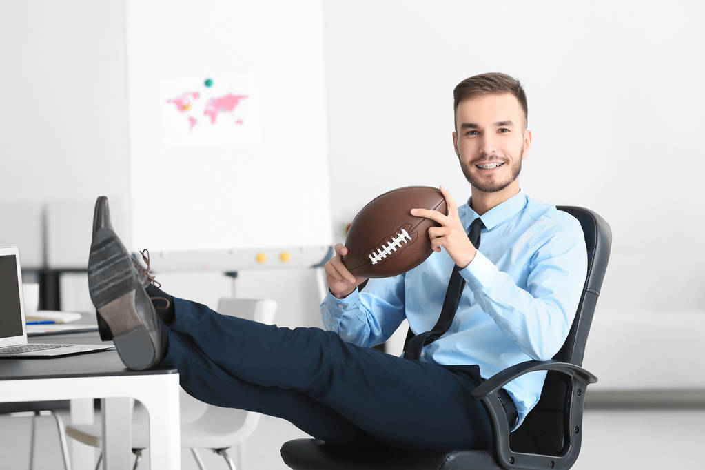 Młody przystojny mężczyzna z piłka do futbolu amerykańskiego w biurze - Zdjęcie, obraz