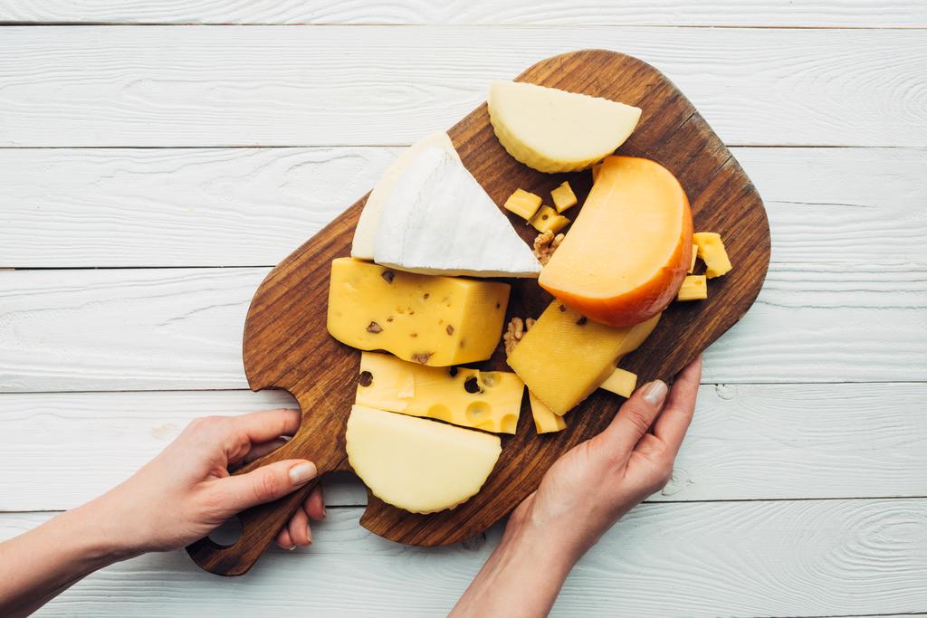 kädet ja valikoituja juustoja puulaudalla
 - Valokuva, kuva