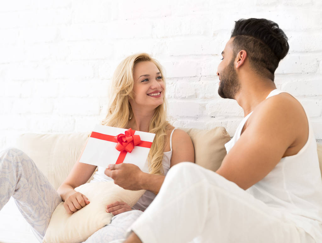 Mladý pár sedí na podlaze polštáře, šťastný úsměv hispánský muž žena drží současné obálky s pásu milenci v ložnici - Fotografie, Obrázek