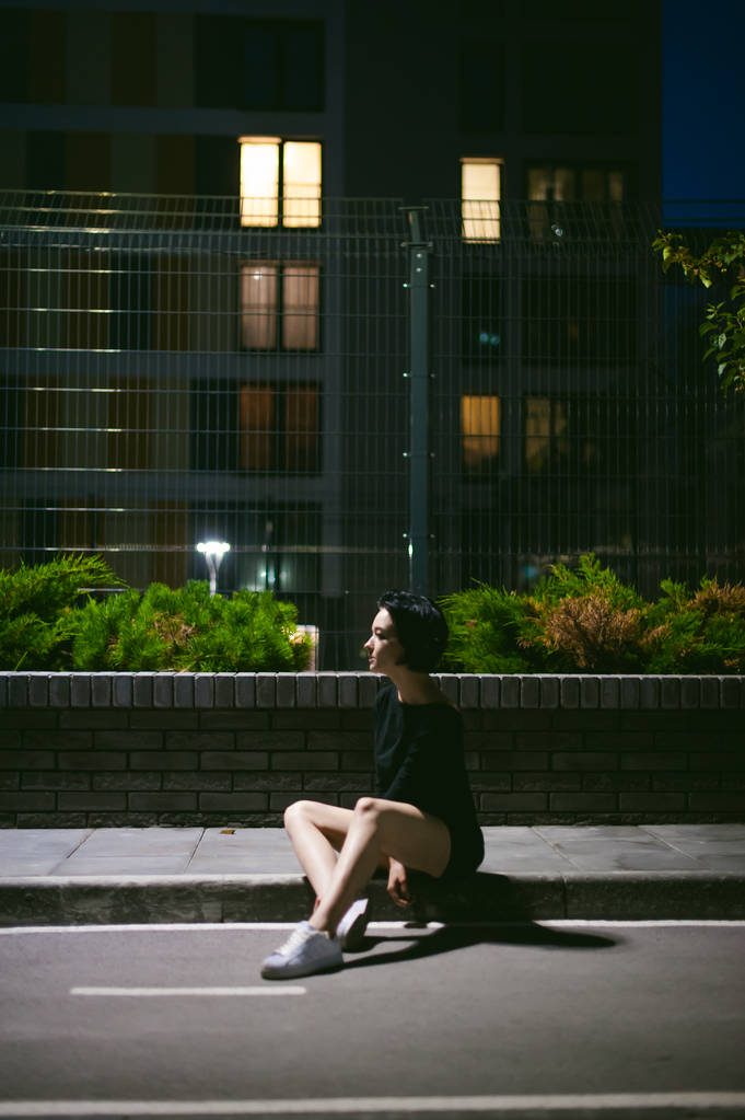 beyaz spor ayakkabı ve kentsel manzara fonunda siyah elbise giymiş güzel ayaklı genç kadın - Fotoğraf, Görsel