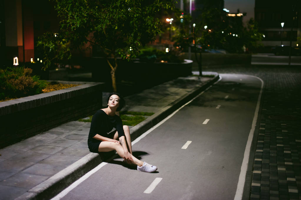 Młoda kobieta z piękne stopy ubrane w białe trampki i czarna sukienka, na tle krajobrazów miejskich - Zdjęcie, obraz