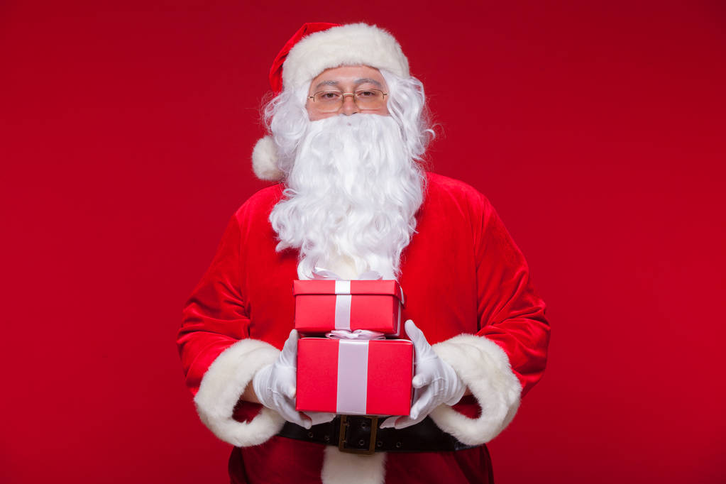 Рождество. Фото Санта-Клауса, дарящего рождественский подарок и смотрящего в камеру, на красном фоне
 - Фото, изображение
