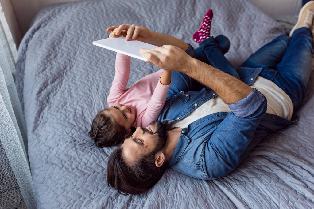 pai e filha usando tablet na cama
 - Foto, Imagem