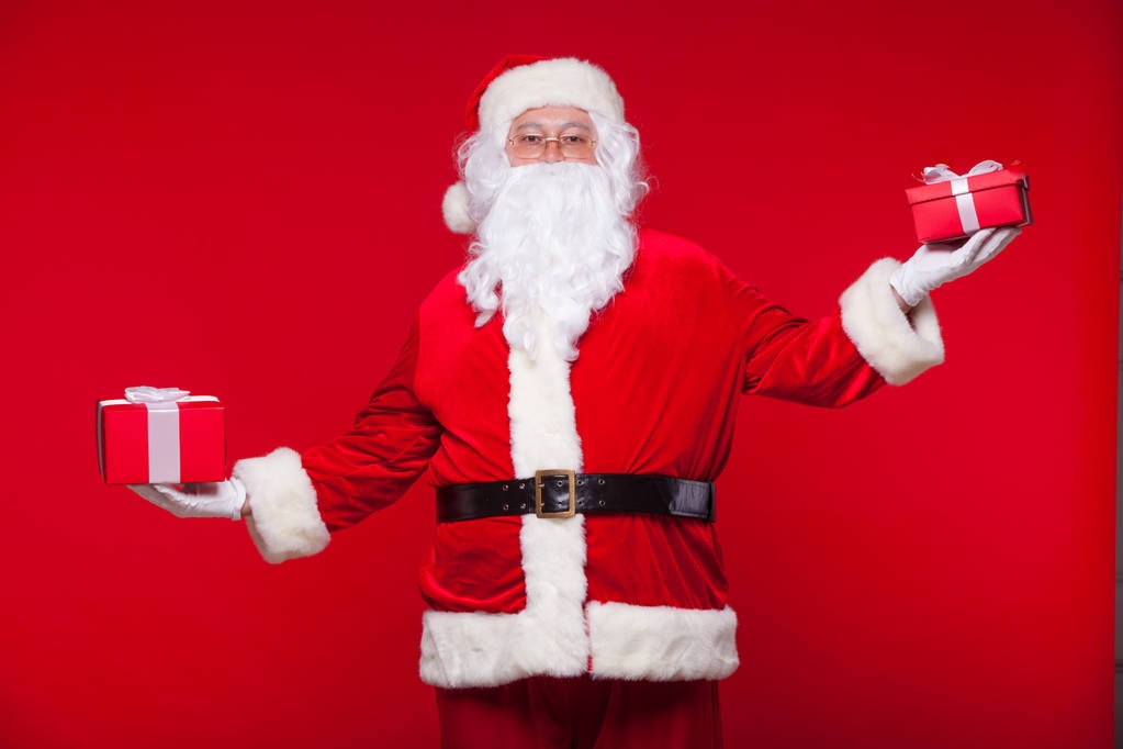 Boże Narodzenie. Mikołaj zdjęcie dając prezent Boże Narodzenie i patrząc na kamery, na czerwonym tle - Zdjęcie, obraz