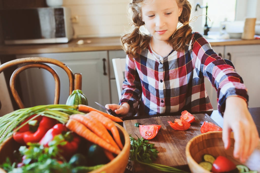 bambina aiuta la mamma a cucinare e tagliare verdure fresche per insalata con il coltello. Bambini che imparano il lavoro di casa in fattoria durante le vacanze estive
 - Foto, immagini