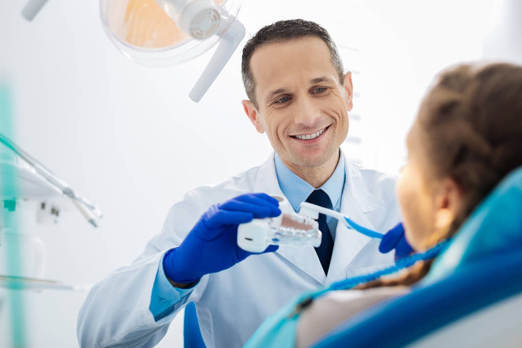 Радісний професійний стоматолог, що показує техніку чищення зубів
 - Фото, зображення