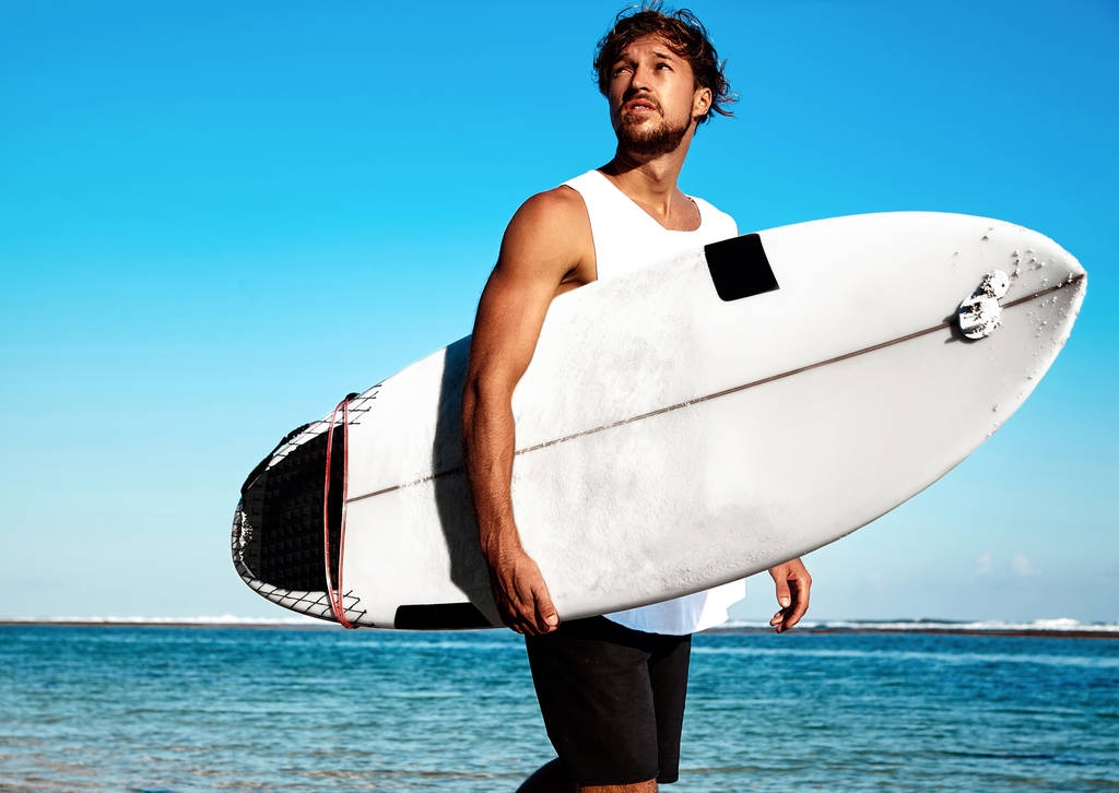 Portrét pohledný bokovky opalovaly módní člověka modelu surfař nosí ležérní oblečení s Surf děje modrý oceán a pozadí oblohy - Fotografie, Obrázek