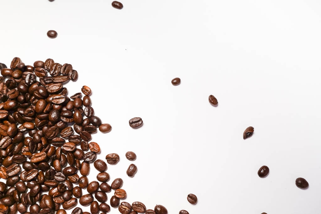 на белом фоне лежат темно-коричневые зерна ароматного кофе
 - Фото, изображение