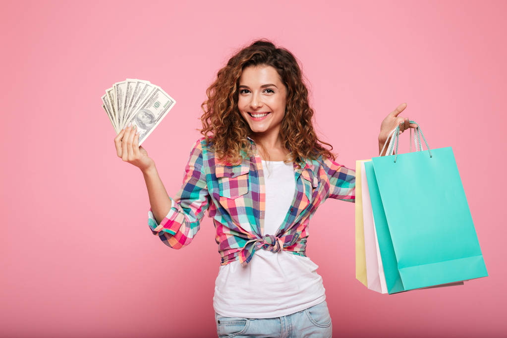 Gelukkige vrouw met geld en boodschappentassen poseren geïsoleerd - Foto, afbeelding