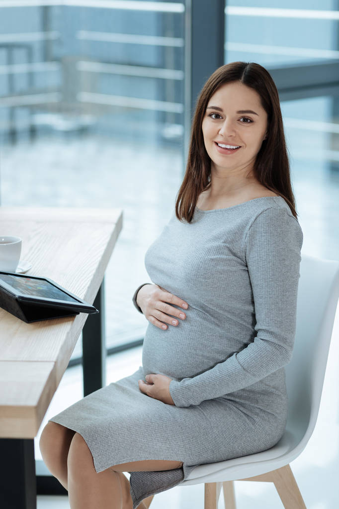 テーブルの上に座っている肯定的な妊娠中の女性 - 写真・画像