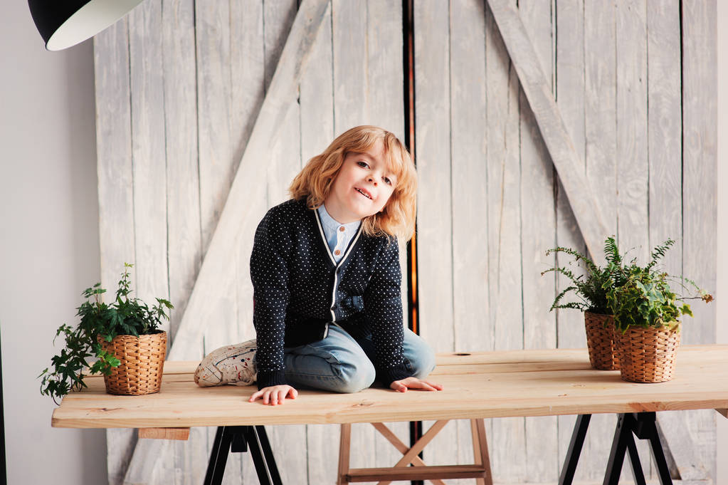 Sisäkuva 5-vuotiaasta pojasta, jolla on pitkät hiukset, istuu pöydällä kotona
 - Valokuva, kuva