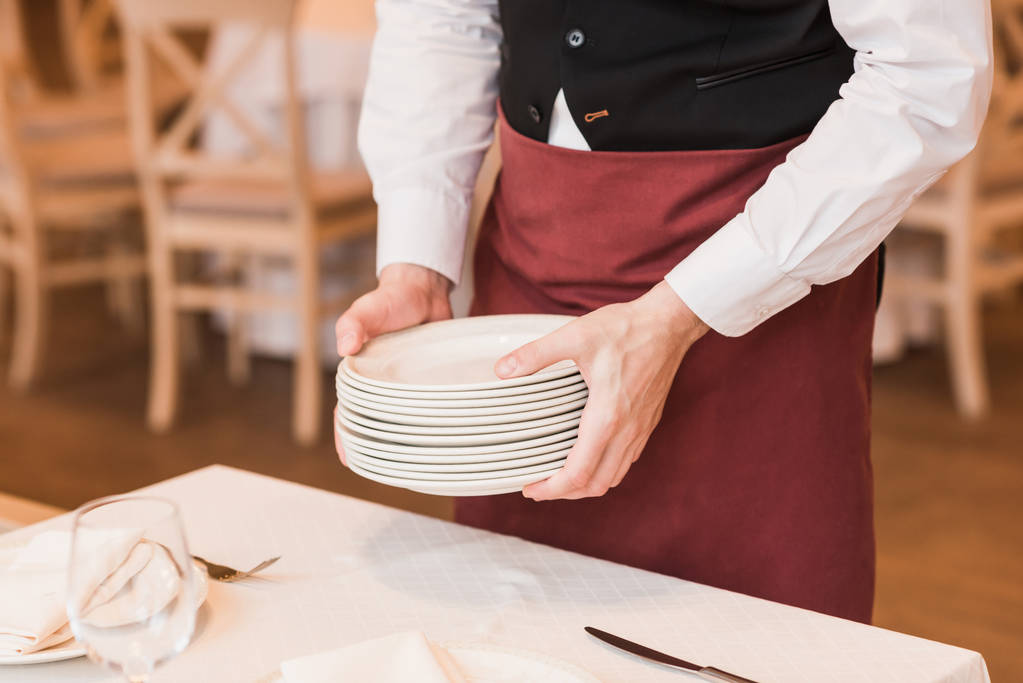 Σερβιτόρος βάζοντας σωρό πιάτα στο τραπέζι - Φωτογραφία, εικόνα