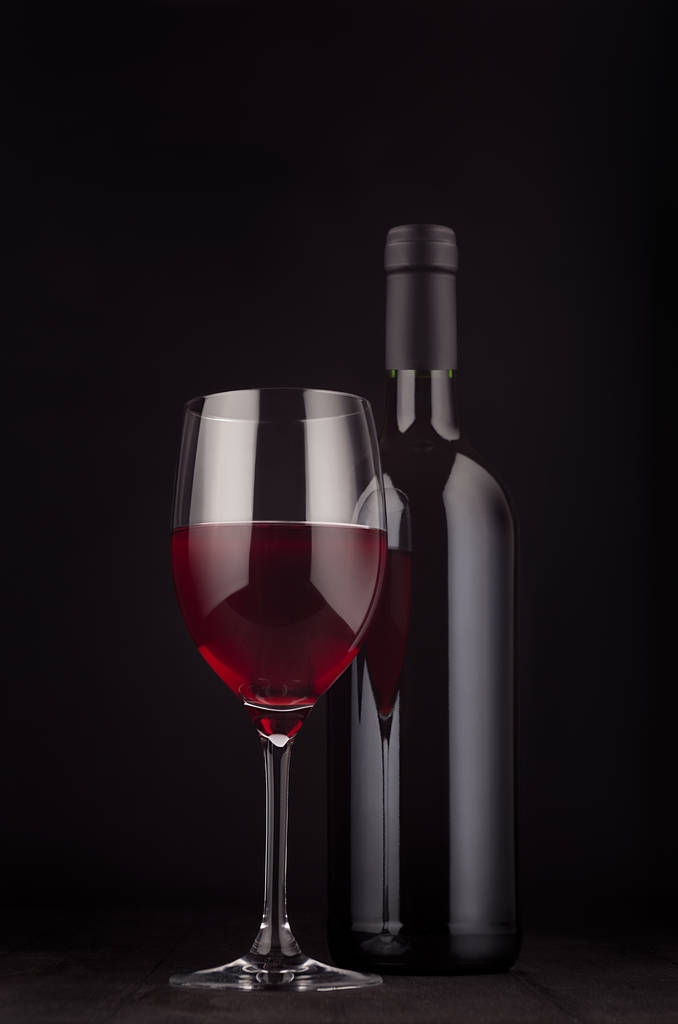 Bouteille de vin rouge et verre à vin maquillée sur un élégant fond en bois noir foncé, vertical
.  - Photo, image