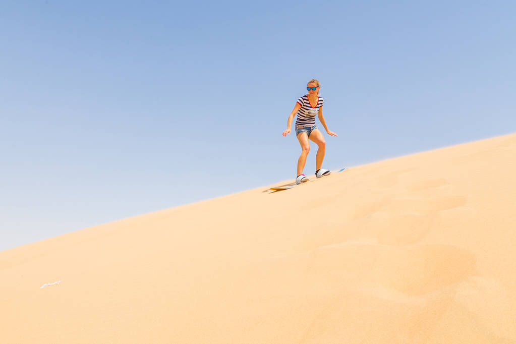 Woman sandboarding down the dune in a desert - Photo, Image