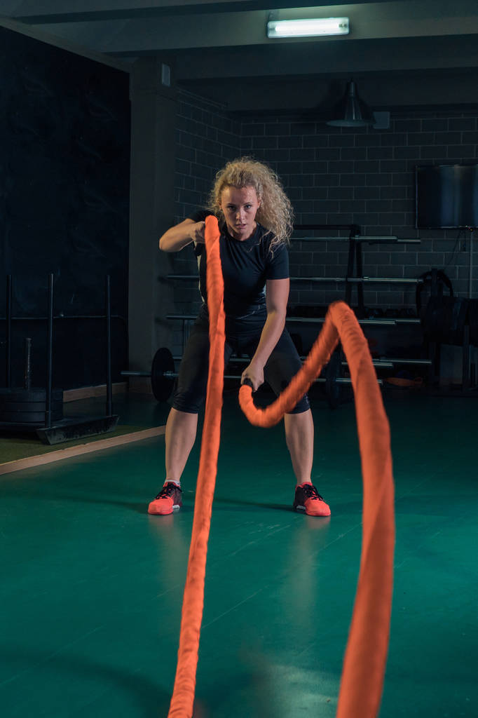 Young strong woman is training with martial ropes in the gym. - Photo, Image