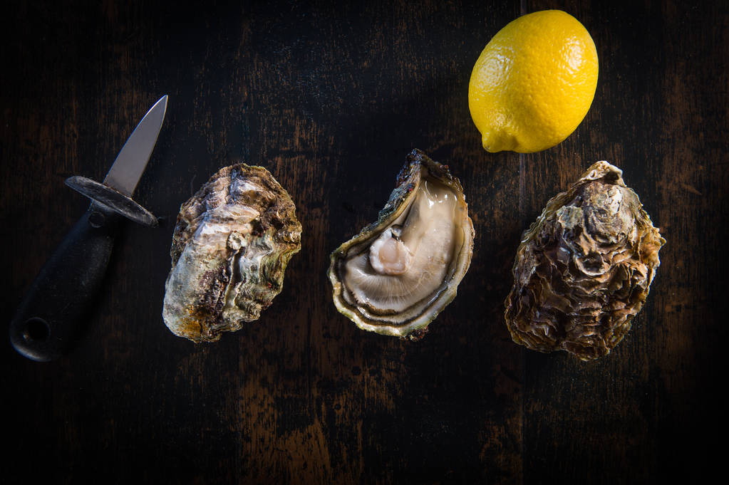Geopende oesters op natuursteen leisteen plaat met citroen en oester mes - Foto, afbeelding