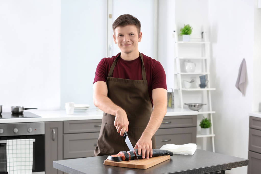 Nuori mies leikkaa tuoretta lohta keittiössä
 - Valokuva, kuva