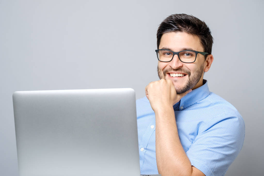 Retrato del joven sonriente sentado en el escritorio con el ordenador portátil
 - Foto, imagen