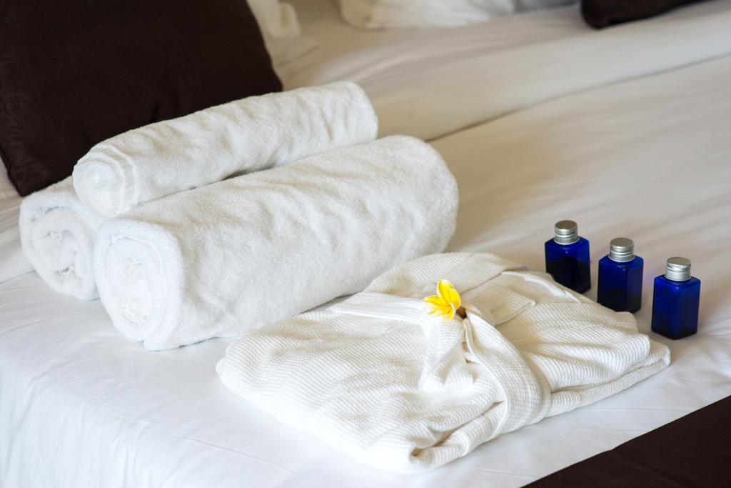 κυλημένες πετσέτες και μπουρνούζι στο κρεβάτι - Φωτογραφία, εικόνα