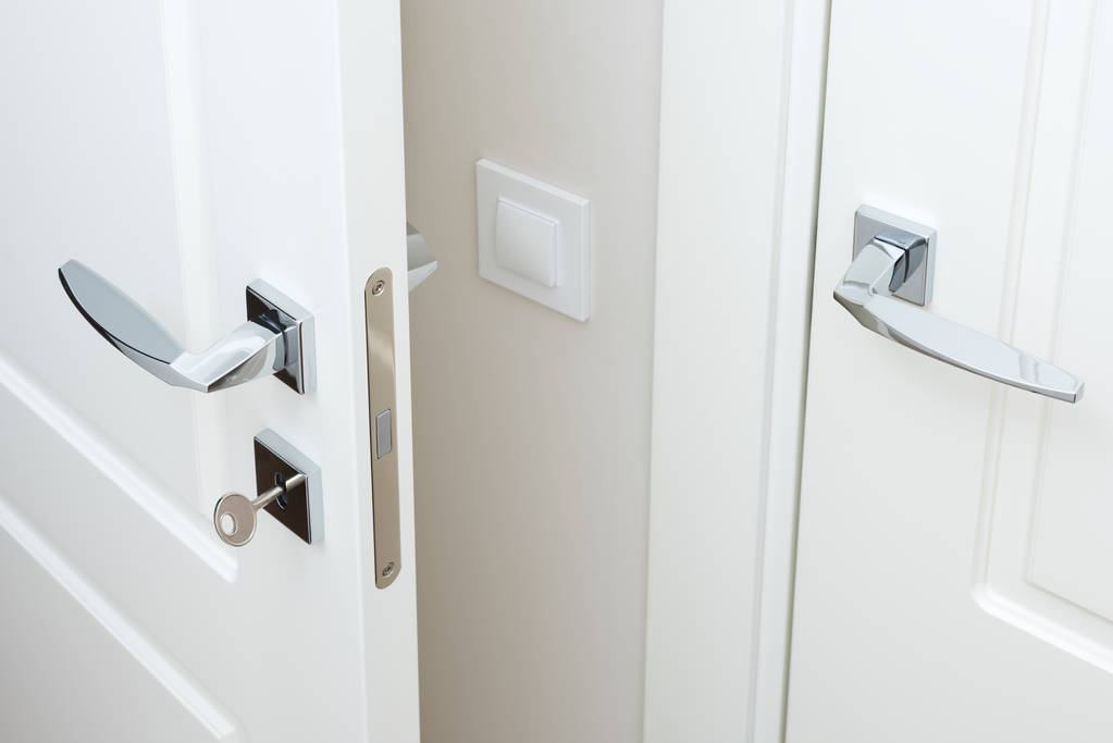 Сучасні хромовані дверні ручки і замок з ключем. Білі міжкімнатні двері крупним планом
 - Фото, зображення