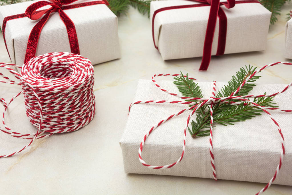 Рождественская подарочная коробка, завернутая в белую ремесленную бумагу и красную ленту на мраморной поверхности. Закрыть
. - Фото, изображение
