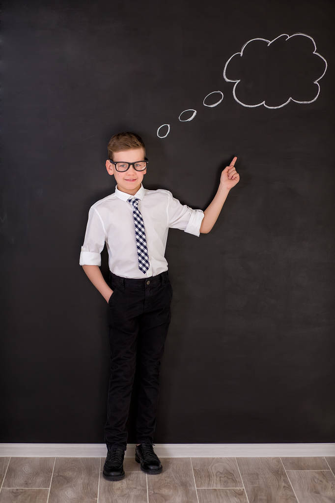 Chłopiec przystojny szkoły w googles biała koszula krawat stojący nieopodal ławce szkolnej z myślenia chmury nad głową. - Zdjęcie, obraz