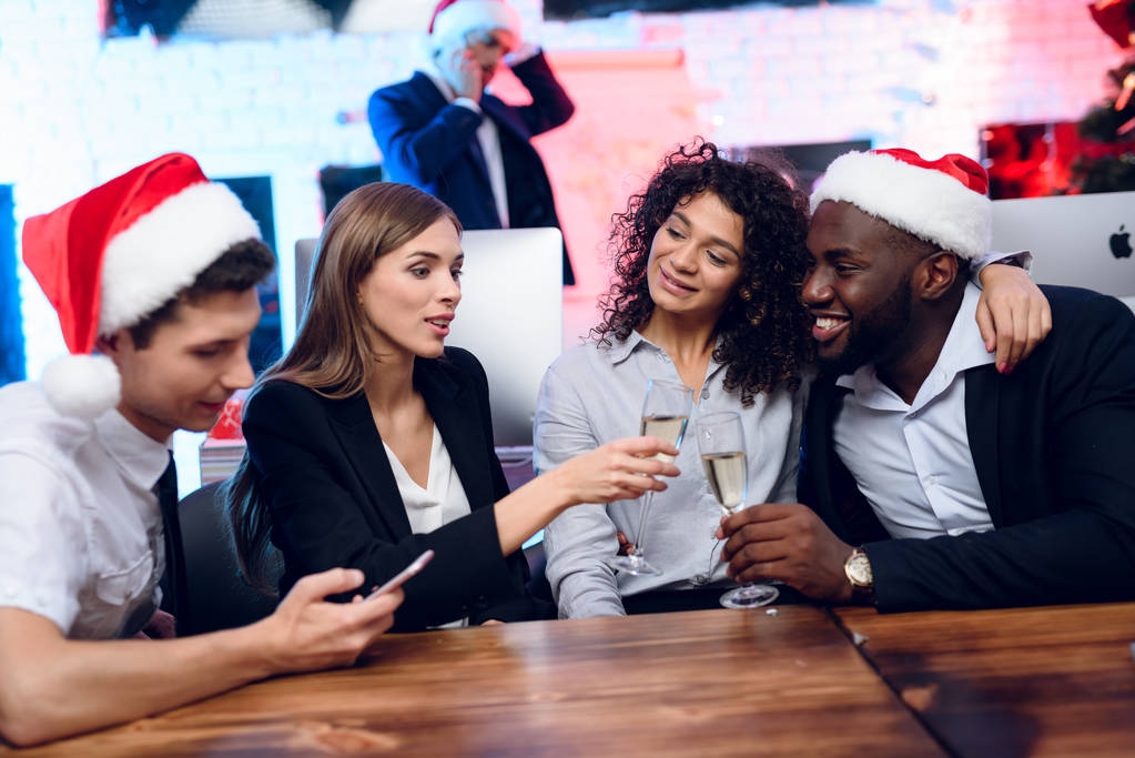 Люди готовятся встретить новый год в офисе. Они сидят с бокалами шампанского в руках и веселятся.
 - Фото, изображение