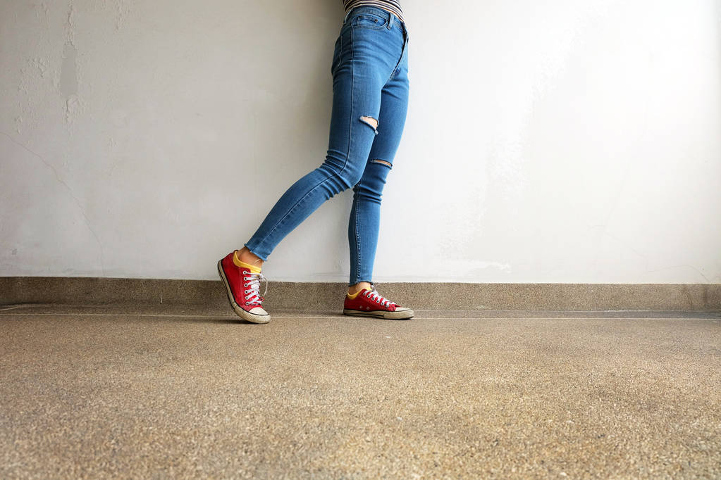 rote Turnschuhe. Frauenbeine in roten Turnschuhen und blauen Jeans auf Bodengrund - Foto, Bild
