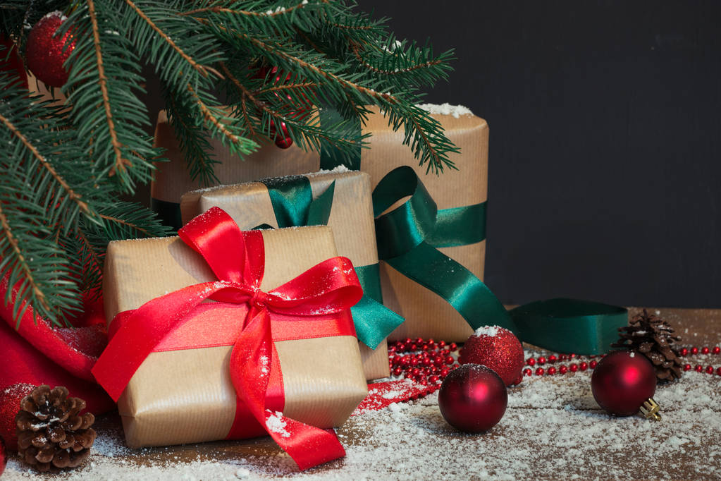 Fondo de vacaciones de Navidad. Regalos con una cinta roja, sombrero de Santa Claus y decoración bajo un árbol de Navidad en una tabla de madera
. - Foto, imagen