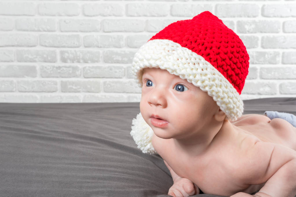 Новорожденный ребенок лежит на животе в шляпе Санта-Клауса
 - Фото, изображение
