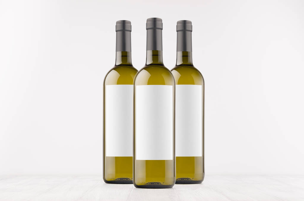 Drie groene wijnflessen met etiketten van de blanco wit op wit houten bord, mock up. - Foto, afbeelding