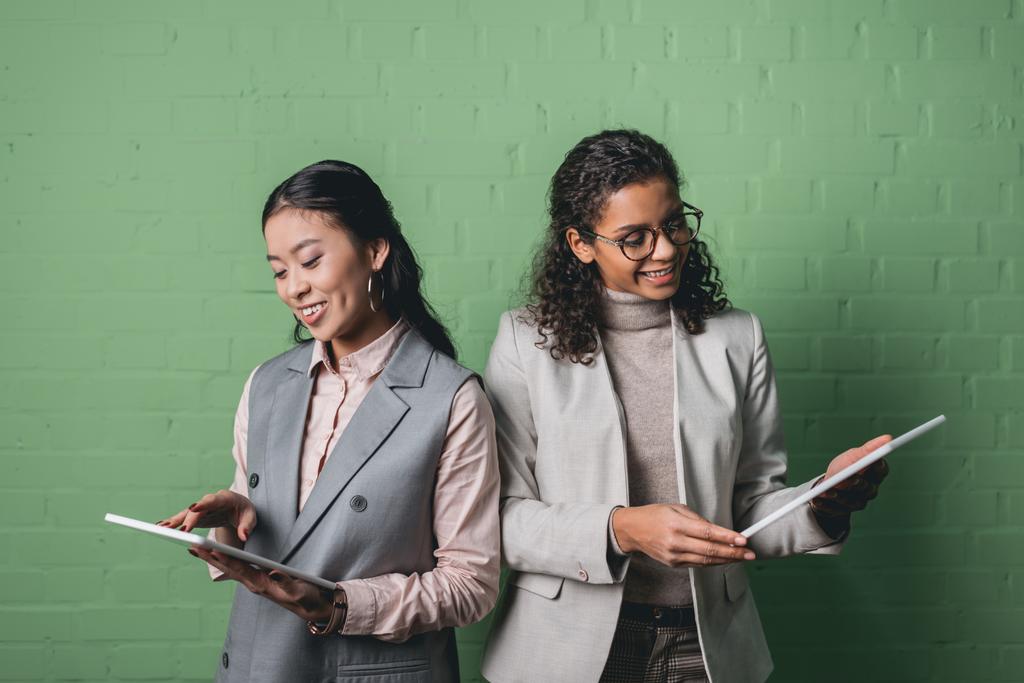 Afrikanische amerikanische und asiatische Geschäftsfrauen mit digitalen Tablets vor einer grünen Wand - Foto, Bild